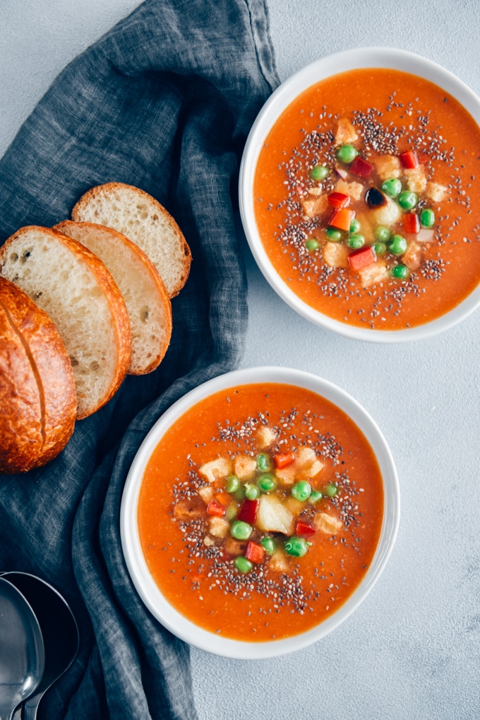 素食番茄汤供应的两个白色碗伴随着面包卷，烤大蒜，油煎面包块和豌豆。