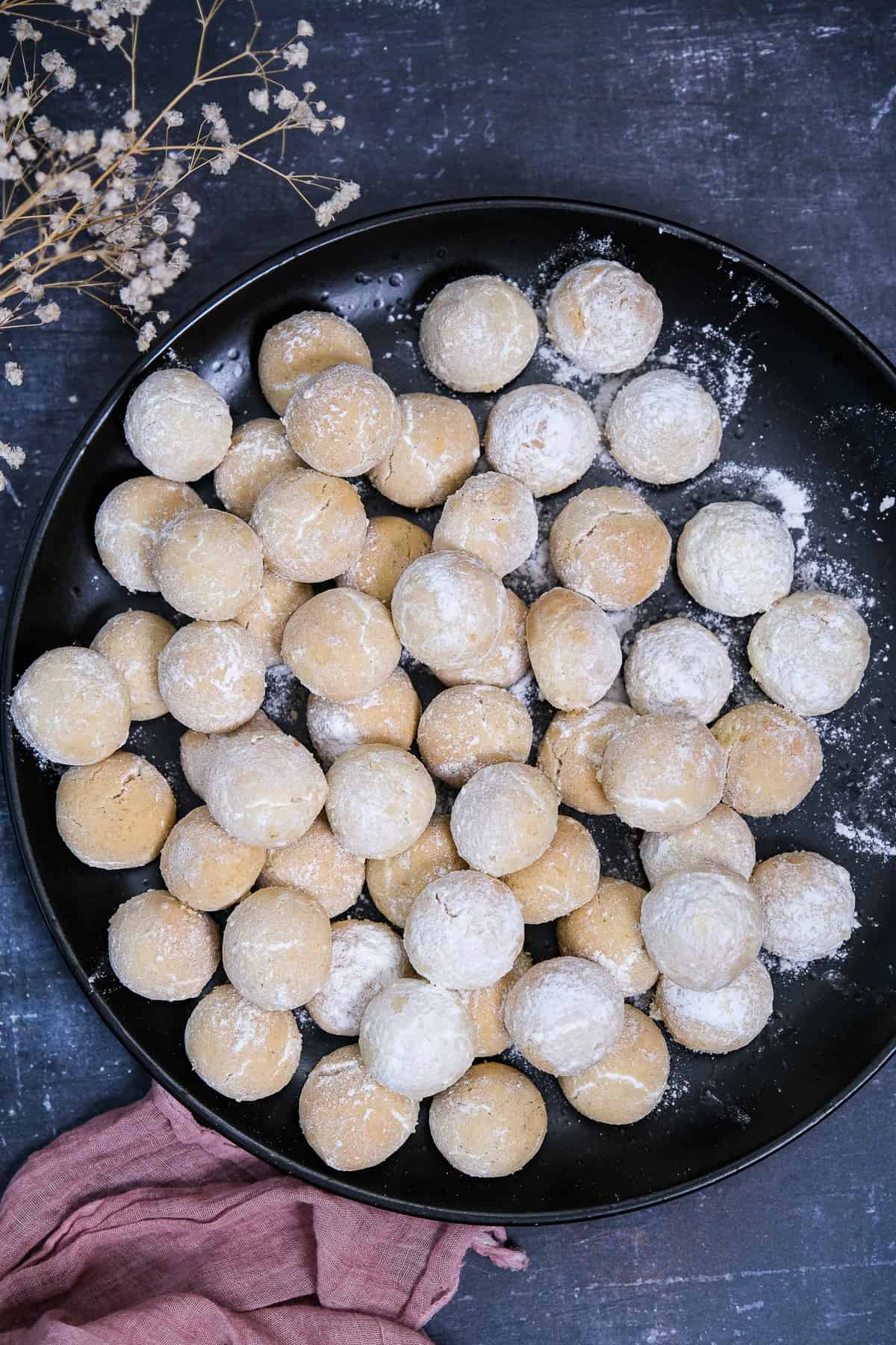 黑色盘子里放着裹着糖粉的迷你融化饼干,旁边放着干花和粉红色的餐巾。