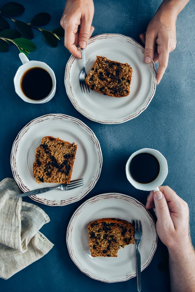 The best Chocolate Chip Banana Bread Recipe. Moist, packed with chocolate chips and tastes like banana. #bananabread #chocolatechipbananabread 两个人在吃早餐,白盘子里盛着巧克力片香蕉面包,还有茶。