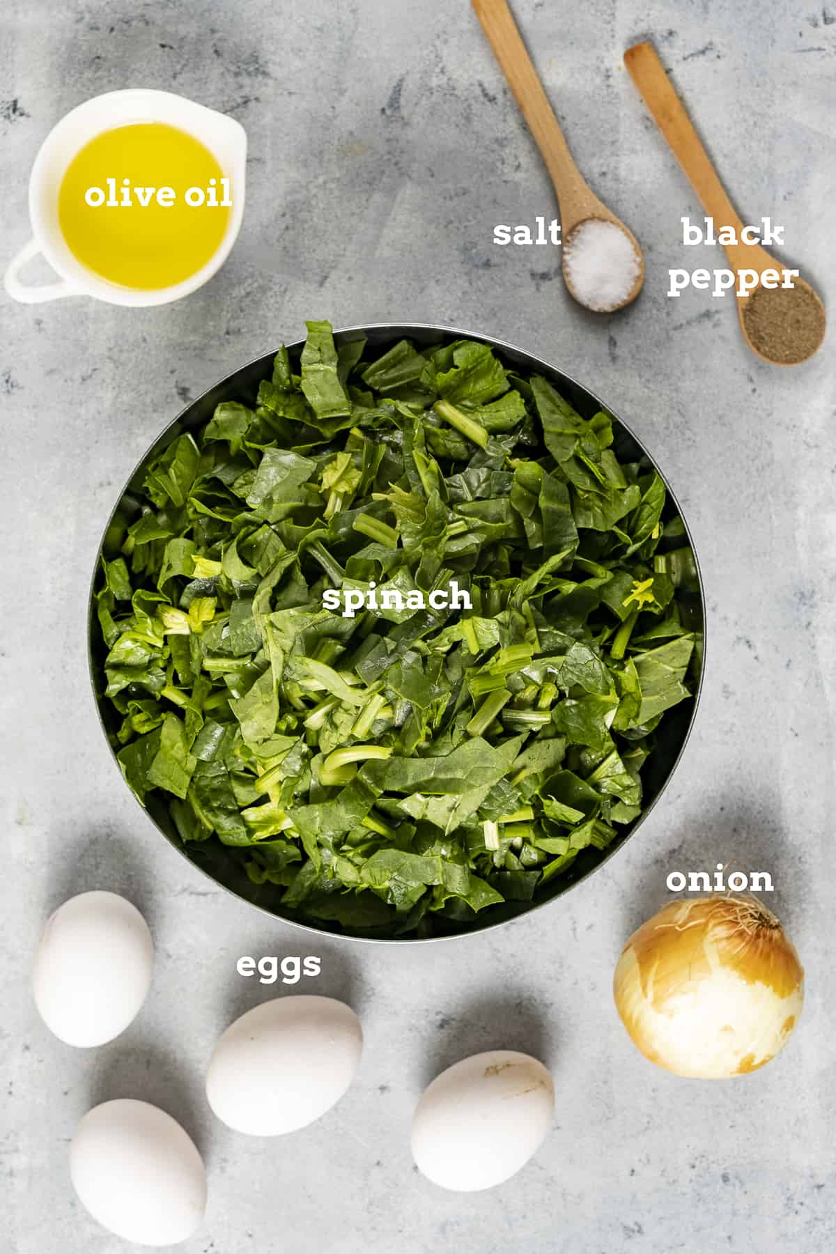 菠菜碎，橄榄油，盐和胡椒，鸡蛋和洋葱在灰色背景上。