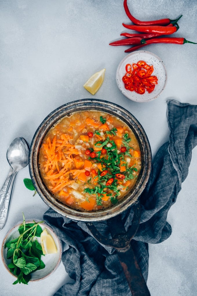 胡萝卜汤用扁豆和米在葡萄酒平底锅装饰用切好的新鲜薄菏和辣椒在从顶视图拍摄的浅灰色的背景。
