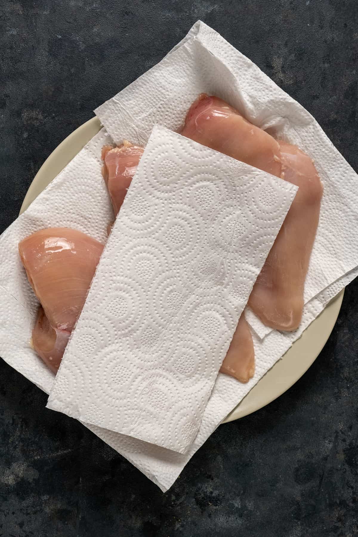 鸡胸肉放在盘子里,上面铺上纸巾,再铺上一张纸巾。