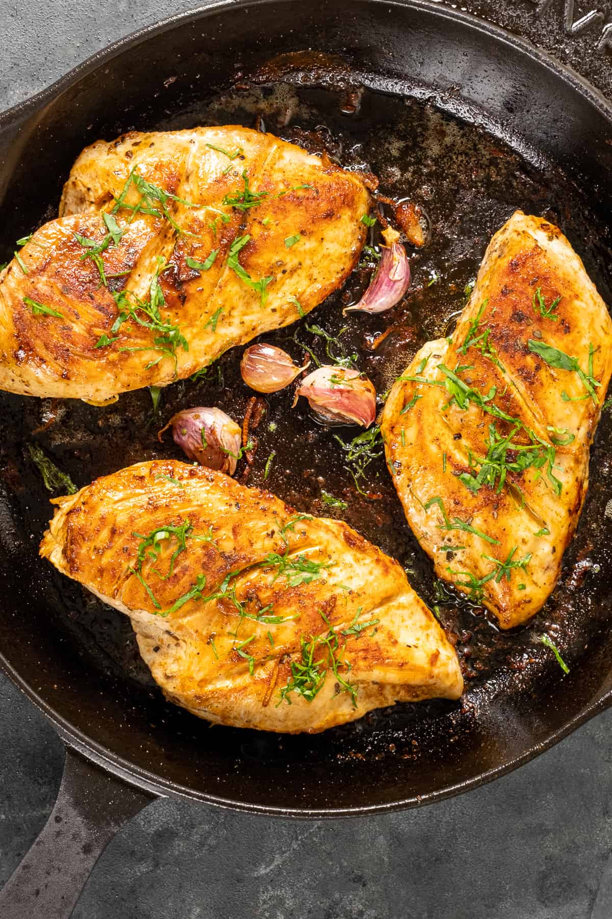 将煮熟的鸡胸肉放入铸铁煎锅中，配以切碎的欧芹和蒜瓣。