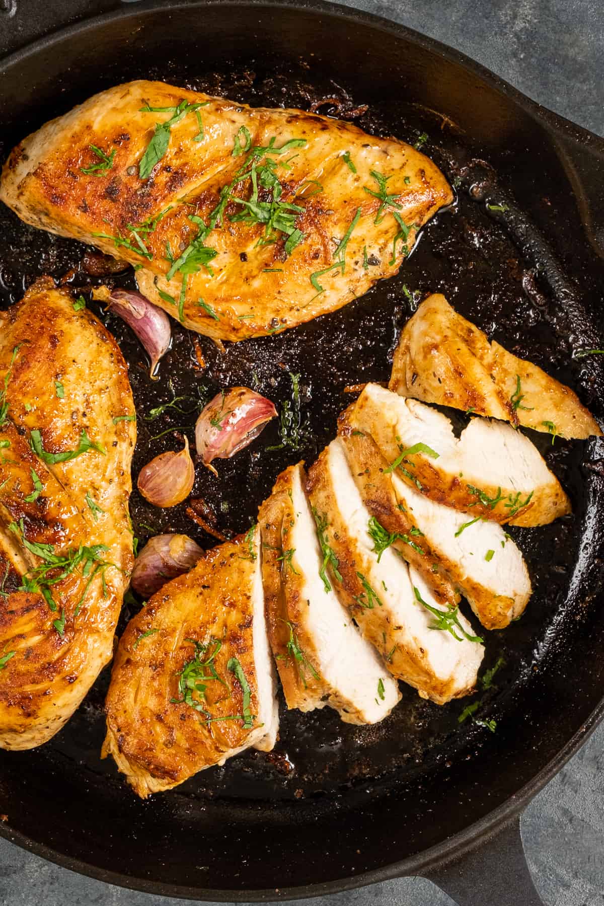 三片金黄色的鸡胸肉，一片切片，放在铸铁锅里，旁边放上切碎的欧芹和蒜瓣。