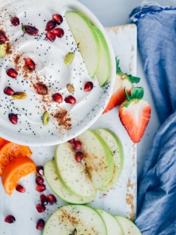 酸奶水果蘸点缀以罂粟种子,石榴假种皮、开心果和肉桂在白色的陶瓷碗在白色的木板。