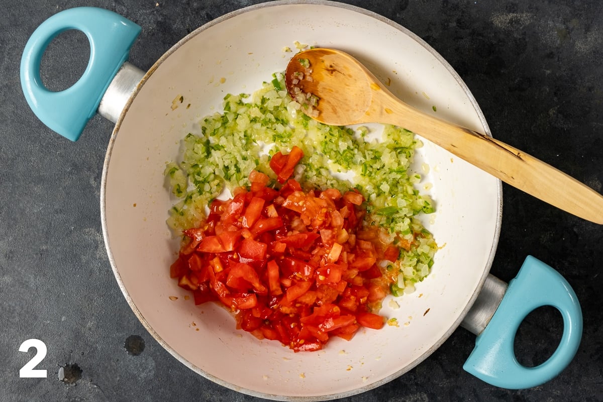 在白色平底锅中放入切碎的西红柿、洋葱和辣椒，并在其中放入木勺。