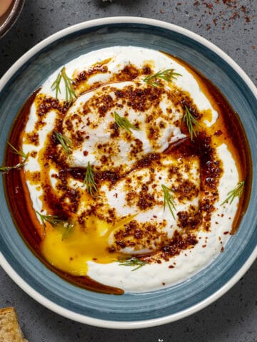 土耳其鸡蛋装在蓝色的碗里，配上辛辣的黄油酱和切碎的新鲜莳萝，背景为深色。