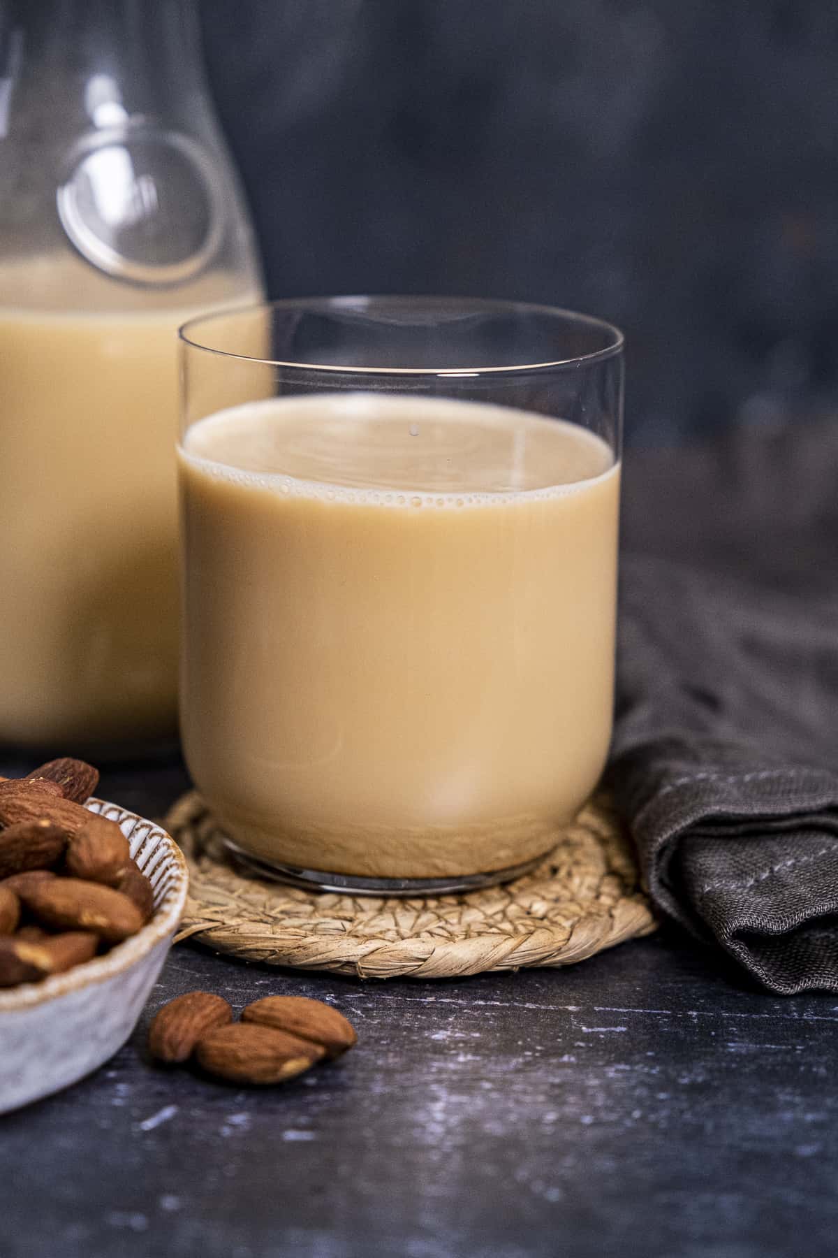 Almond milk with a nice light brown color in a glass and in a bottle and whole almonds on the side.