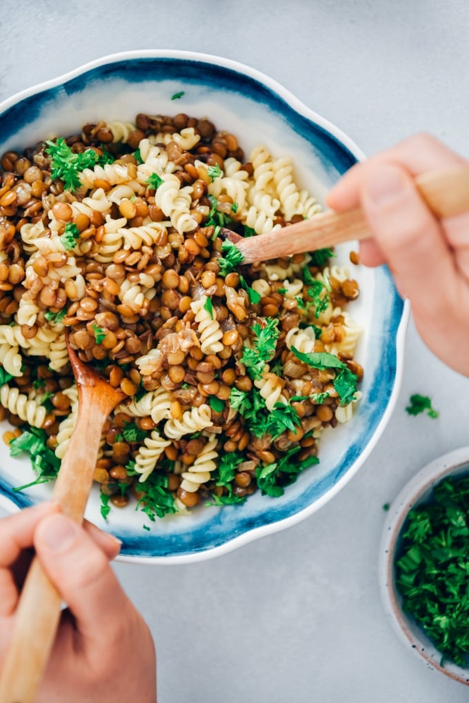 Vegan bolognese using lentils is a wonderful alternative to classic bolognese sauce. This is the most innocent AND TASTIEST pasta sauce ever! #veganrecipe #veganbolognese #lentilbolognese #lentilrecipes 女人用木勺搅拌扁豆肉酱和意大利面。