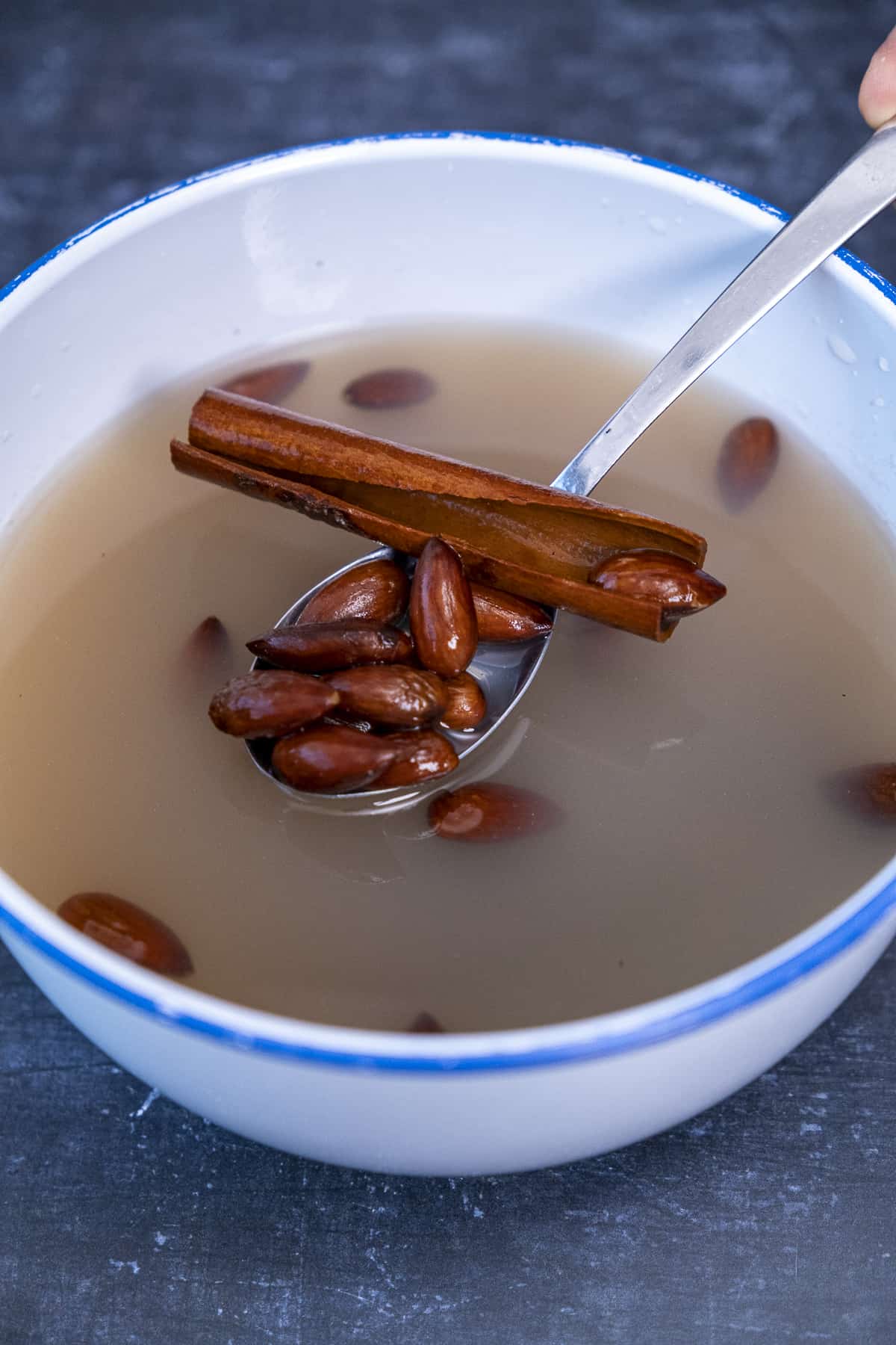 Roasted almonds and a cinnamon stick in a spoon over the soaking bowl.