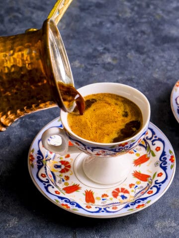 一个土耳其铜制咖啡壶，将咖啡倒入传统的杯子中。
