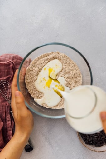 倾吐牛奶的妇女入在一个玻璃碗的干燥成份混合物制造蓬松卵粉薄煎饼。