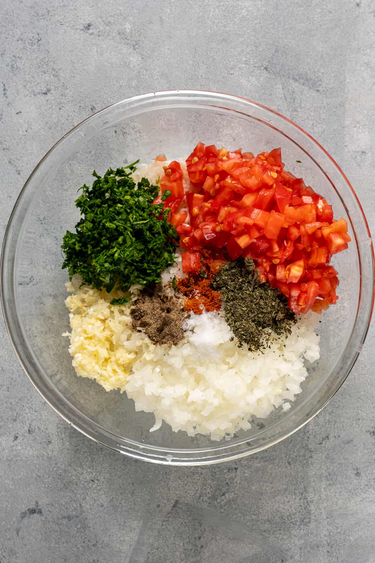 米饭,切碎的大蒜,洋葱,西红柿,欧芹和香料放入一个玻璃搅拌碗中。