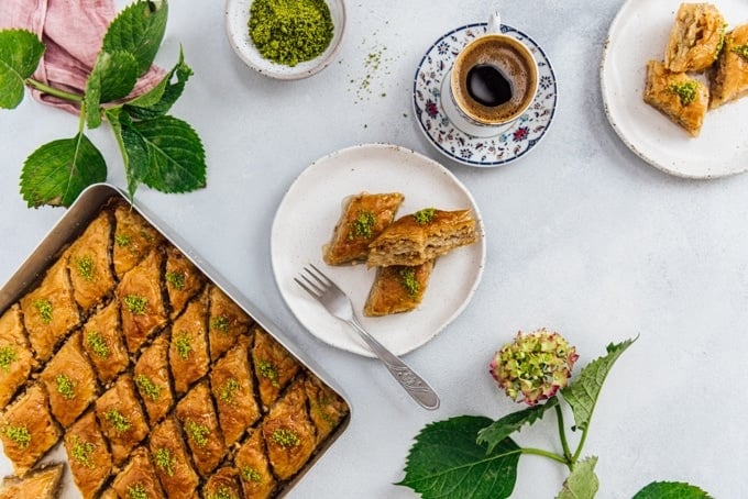 传统土耳其咖啡杯中的土耳其咖啡，陶瓷盘上的两片土耳其果仁蜜饼，烤盘上满是新做的果仁蜜饼