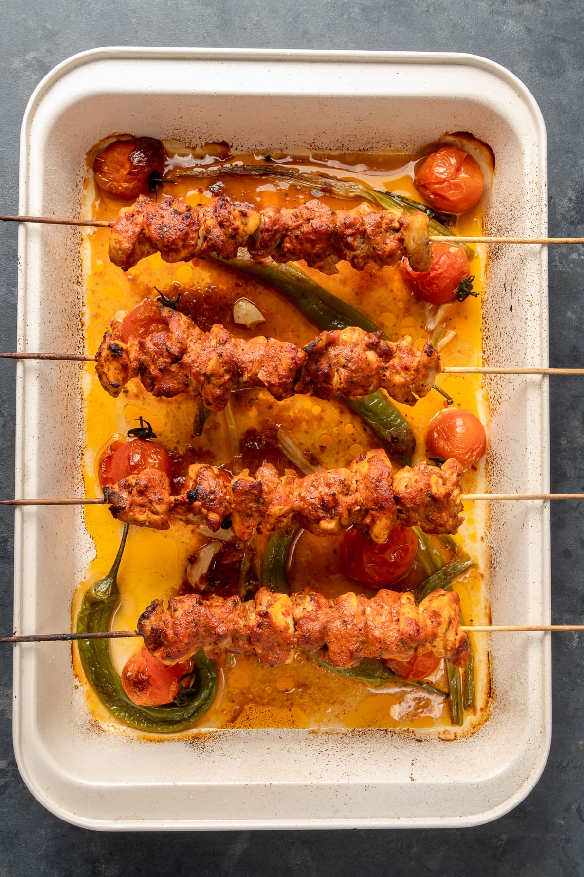 烤炉里的烤鸡串放在一个长方形的烤盘的边缘，西红柿、青椒和葱都在锅里。