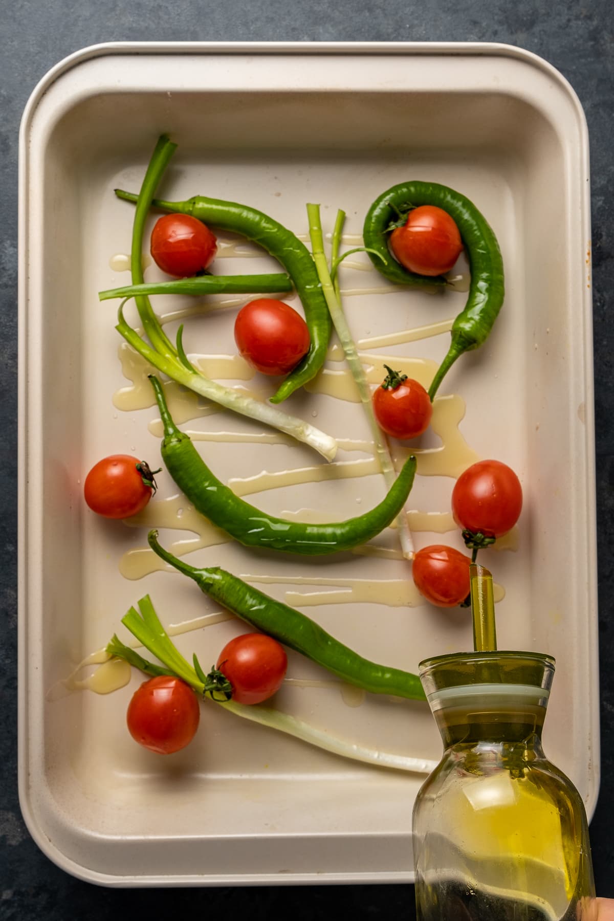 将一瓶橄榄油淋在烤盘里的番茄、青椒和葱上。
