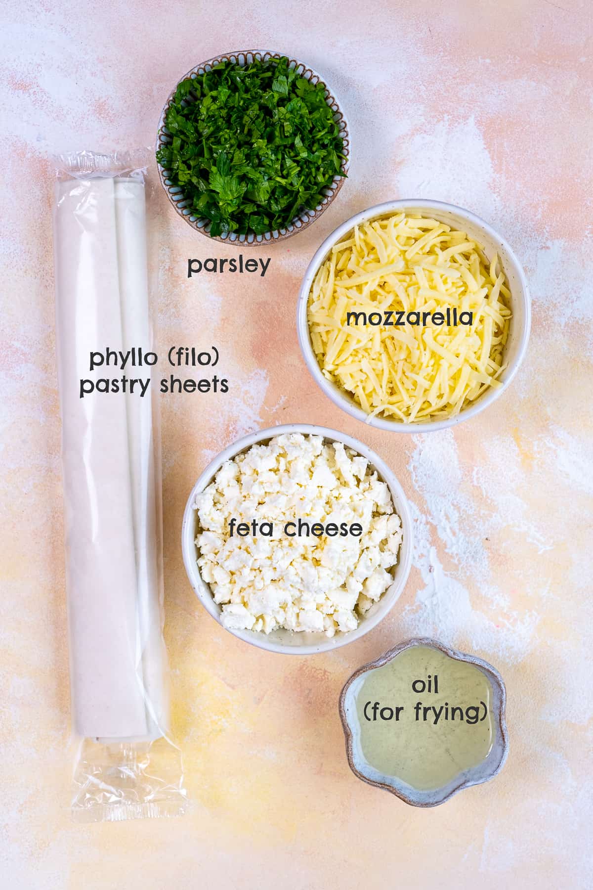 菲罗面团、磨碎的马苏里拉奶酪、碎菲达奶酪、欧芹和油放在不同的碗里，背景淡一点。