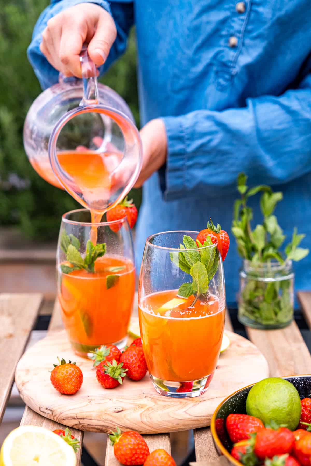 一个女人用大水罐把草莓柠檬水倒进高脚杯里。