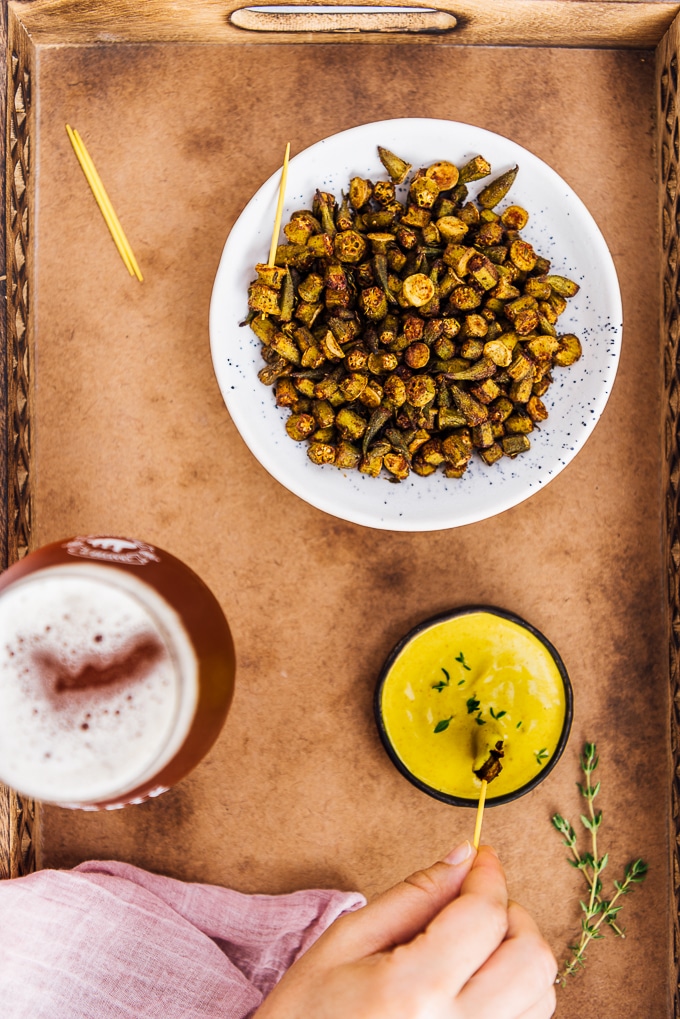 Oven roasted Okra Recipe is for those who hate okra. These crispy roasted okra chips will become their new favorite snack. Healthy and incredibly tasty! #roastedokra #okrarecipe #healthysnack 烤秋葵片配姜黄芝麻酱和一杯啤酒。