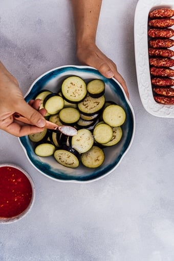 用手把盐撒在瓷碗里切好的茄子上，旁边放上自制的肉丸。