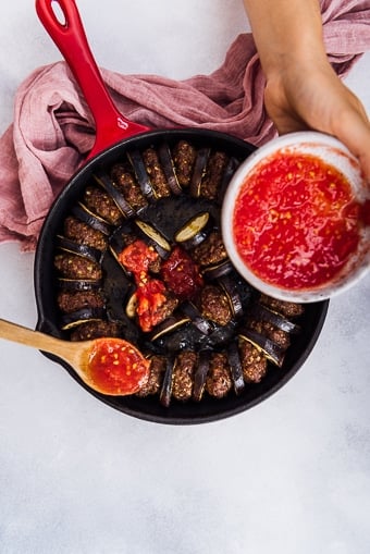 用手把番茄泥倒在烤茄子片和铁锅里的肉丸上。
