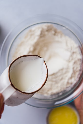 用手将牛奶从迷你牛奶罐中倒入玻璃碗中的面团混合物中。