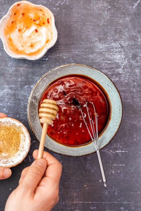 一只手加入蜂蜜入有蜂蜜浸染工具的辣椒酱碗。