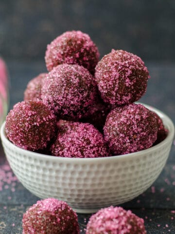 Chocolate truffles with biscuits coated with colored sugar in a white bowl on a dark background.
