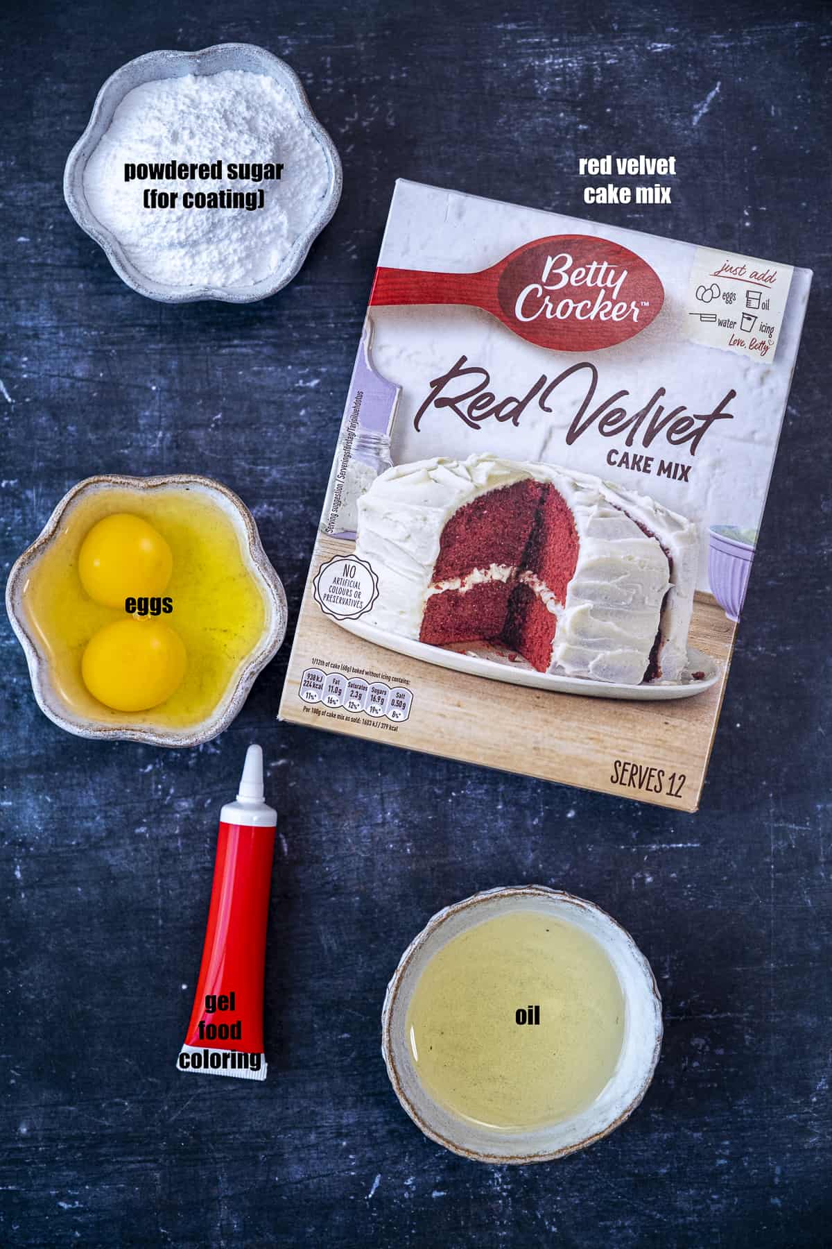 一盒红色天鹅绒蛋糕粉,鸡蛋,糖粉,油和一管黑色背景的红色食用色素。
