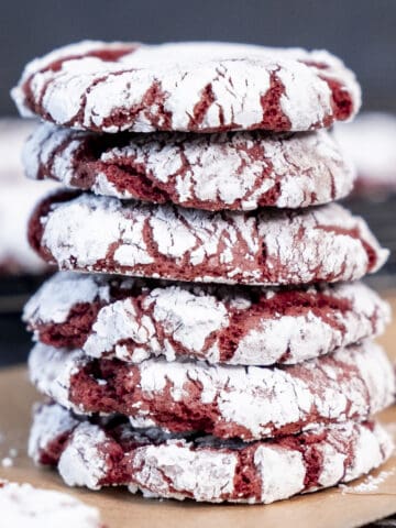 A stack of red velvet crinkle cookies on a baking paper with a dark background.