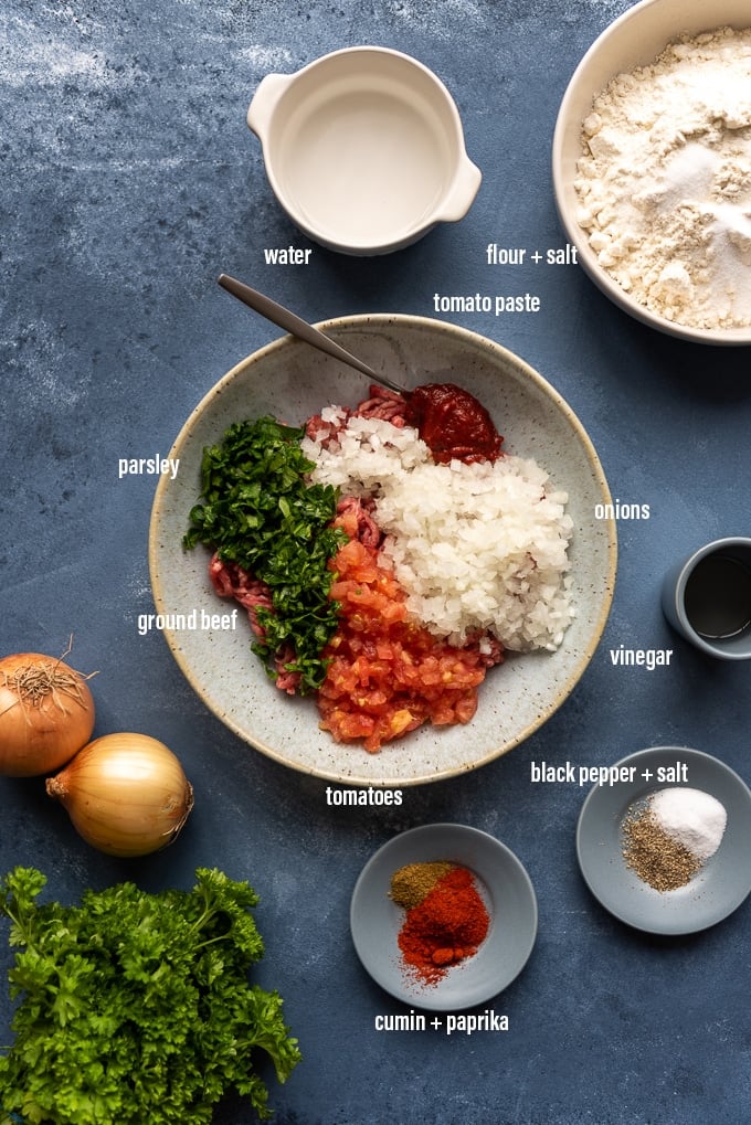 Lahmajun食谱成份包括磨碎的牛肉，洋葱，西红柿，番茄酱，荷兰芹，香料，醋，面粉和盐在深灰色背景上。