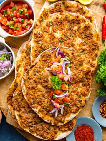 手lahmacun,切洋葱,西红柿沙拉和香料在木板上。