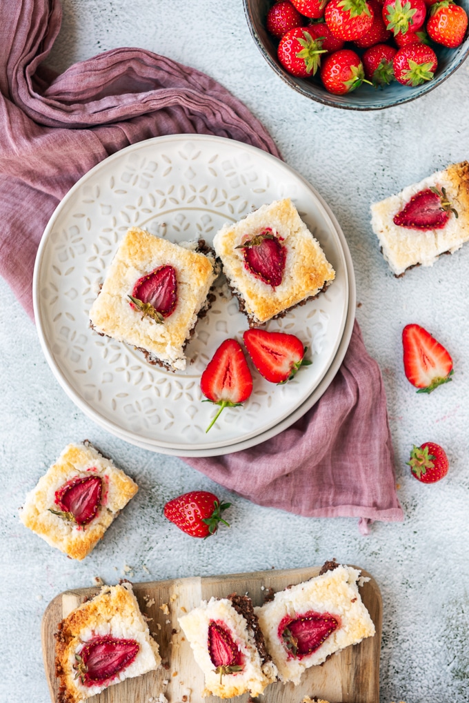 两片切片与巧克力底部和草莓顶部的椰子冰正方形在轻的背景拍摄的白色陶瓷板材。新鲜的草莓和一个木服务板陪同。