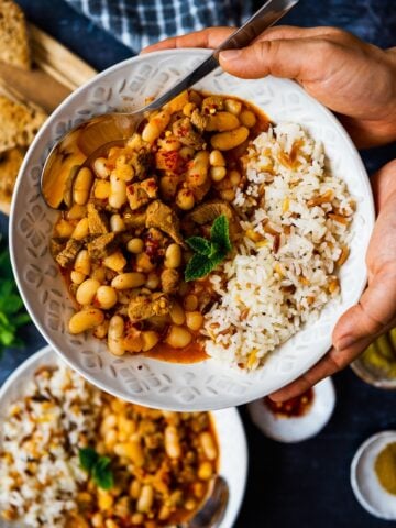双手捧着一碗土耳其白豆炖羊肉和米饭抓饭放在一边。