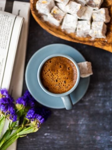土耳其咖啡装在灰色的咖啡杯里，配以土耳其软糖、野花和黑色背景上的报纸。