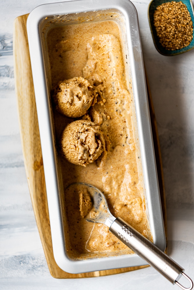 芝麻酱杏仁奶冰淇淋装在面包蛋糕罐中，冰淇淋勺和芝麻放在旁边。