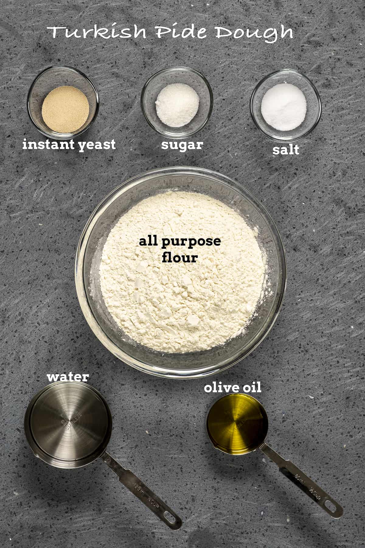 面粉，酵母，糖，盐，水和橄榄油在灰色的背景上。