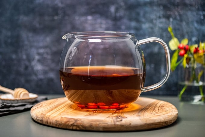 玫瑰果茶，放在木板上的玻璃壶里，配以蜂蜜勺和新鲜的玫瑰果