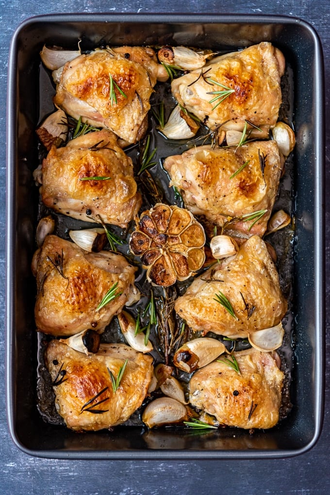 金黄色酥脆的烤鸡腿，配上大蒜和迷迭香，放在长方形的平底锅里