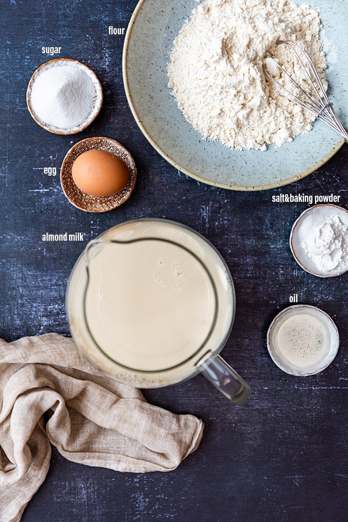 杏仁牛奶在一个罐子，鸡蛋，油，面粉，糖和发酵粉在碗在一个黑暗的背景。