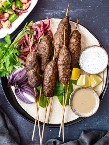 Kofta Kebab在Lavash上，旁边有Sumac洋葱，Tahini酱和酸奶酱。