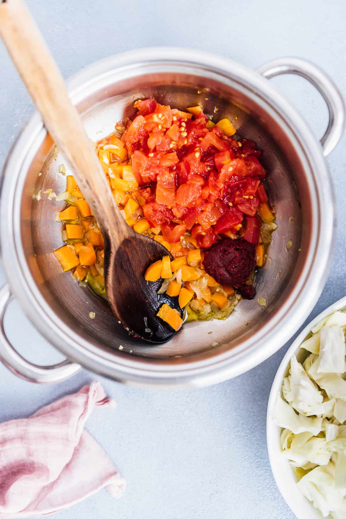 洋葱，胡萝卜，碎番茄和番茄酱在锅里煮，里面有一个木勺。
