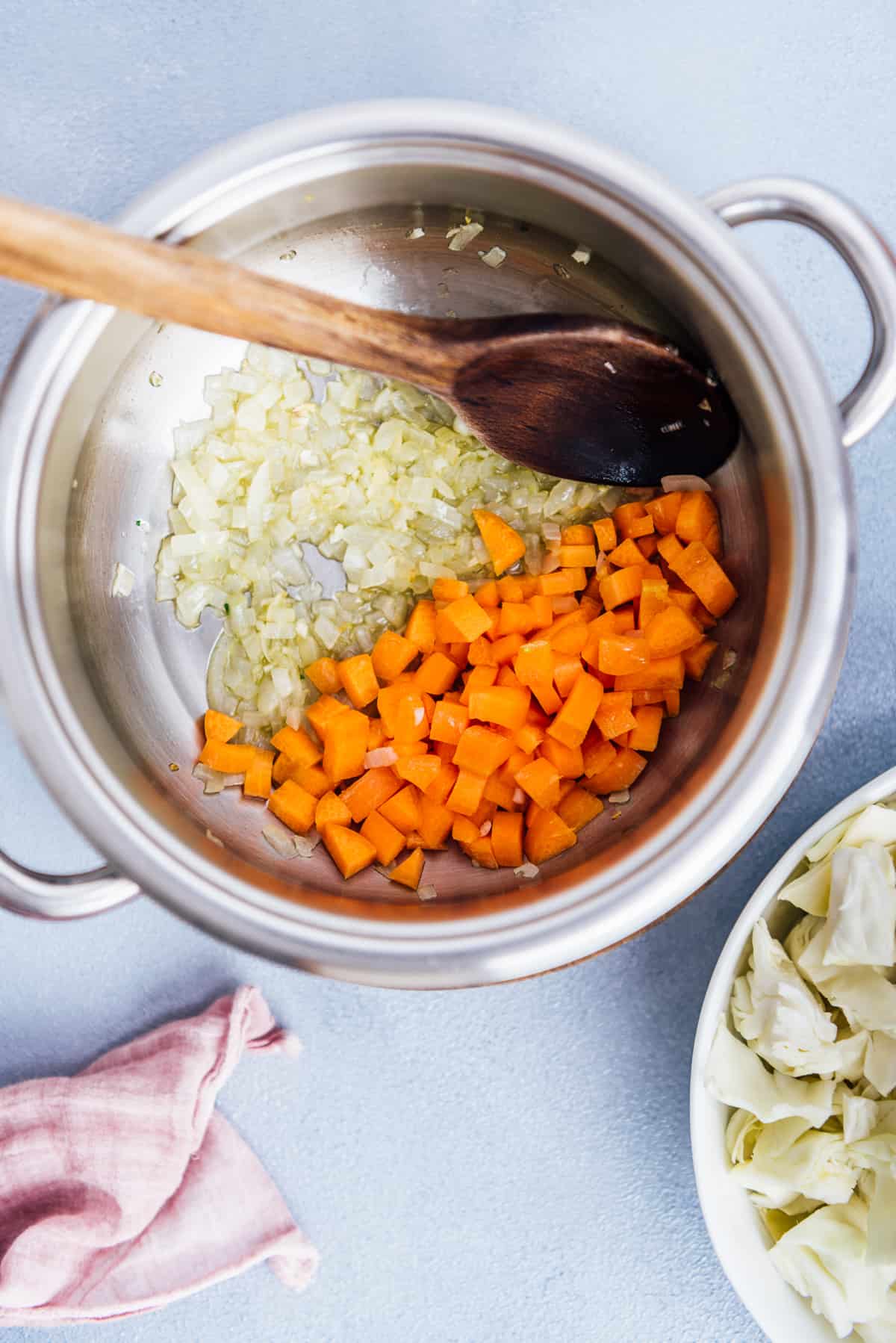 洋葱和胡萝卜在锅里煮，里面有一个木勺。