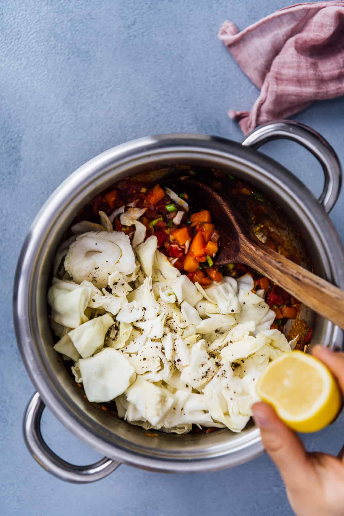 一只手把柠檬挤在锅里煮的卷心菜汤上，锅里有一个木勺。