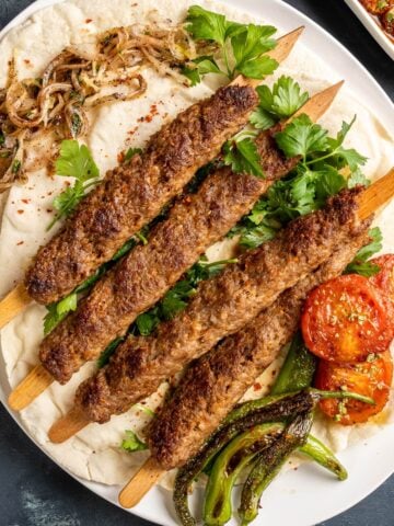Adana Kebab串于Lavash与欧芹，烤蕃茄和青椒。