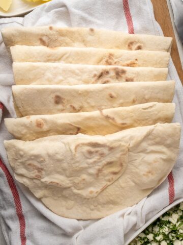 在干净的白色厨房毛巾的Lavash面包。在一个白色卵形板材的黄油在上面和荷兰芹和希腊上在另一个白色卵形板材在底部。