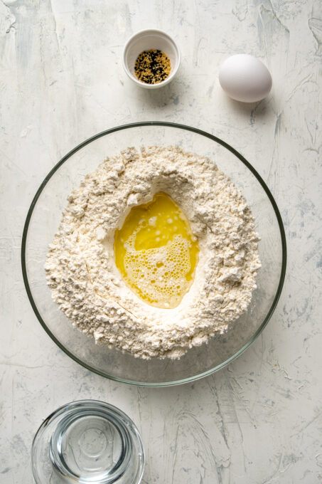 面粉，牛奶和橄榄油在一个大玻璃搅拌碗和水，芝麻和鸡蛋在一边。