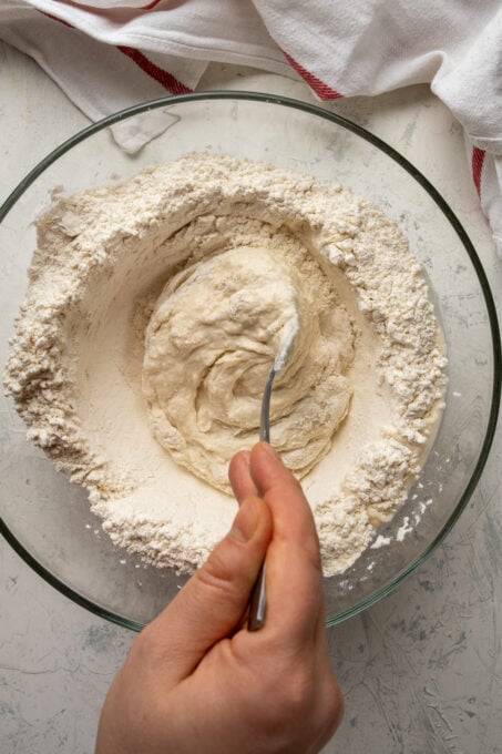 用叉子将面粉和酵母混合物与水混合的手。