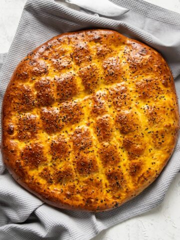 Newly baked pide bread with sesame seeds on a grey kitchen towel.