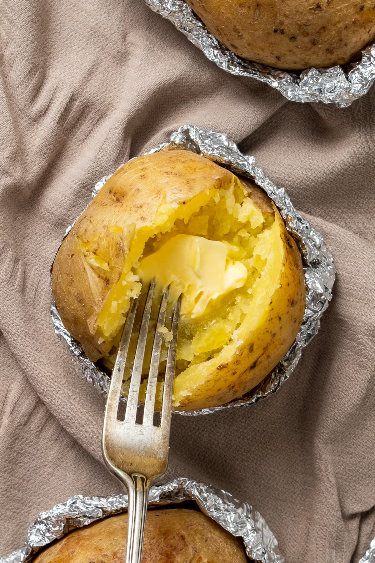 在烤土豆中加入黄油，并在其中放入叉子。